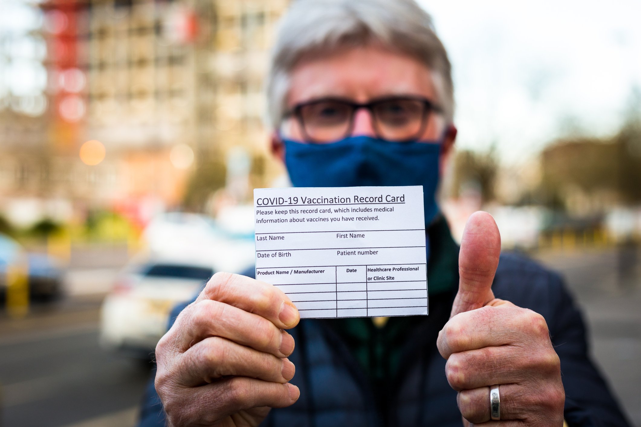 A man holds up a coronavirus vaccine record card while giving a thumbs up.