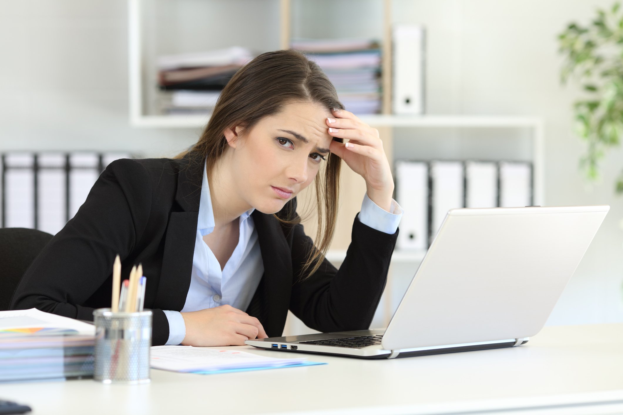 A young female office worker at her laptop, glancing at the camera with a frown.