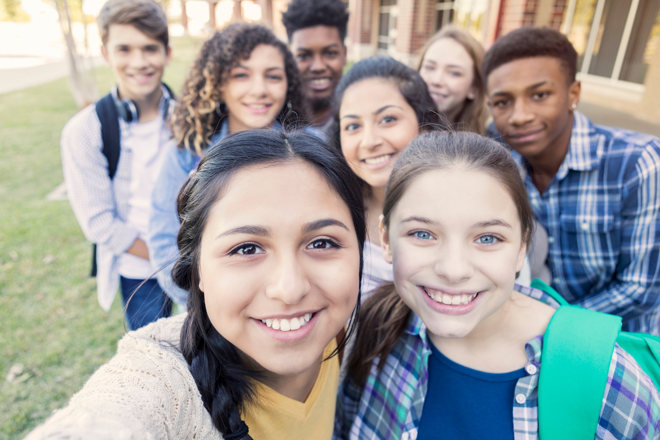 A group of teens smile at into the camera as one takes a selfie.