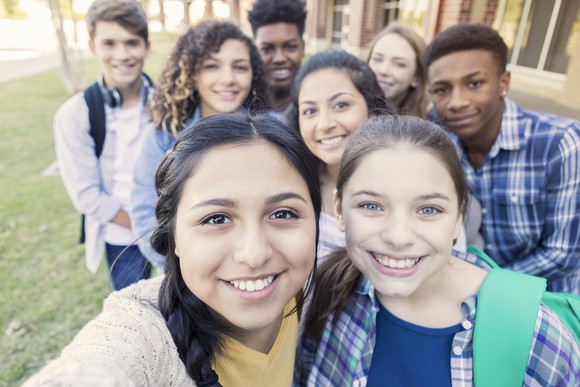 A group of teens smile at into the camera as one takes a selfie.