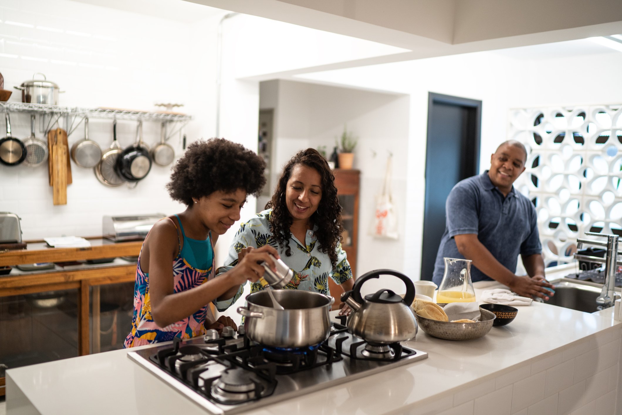Child adding spice to pot while cooking with parents