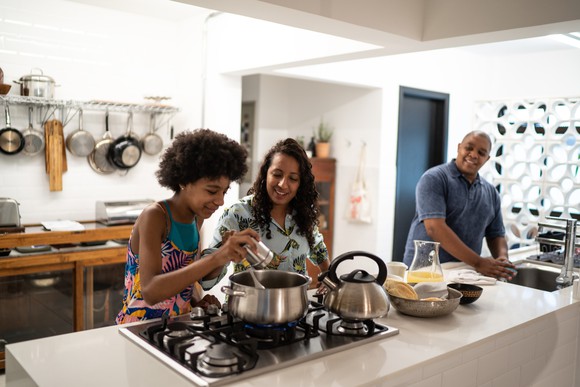Child adding spice to pot while cooking with parents