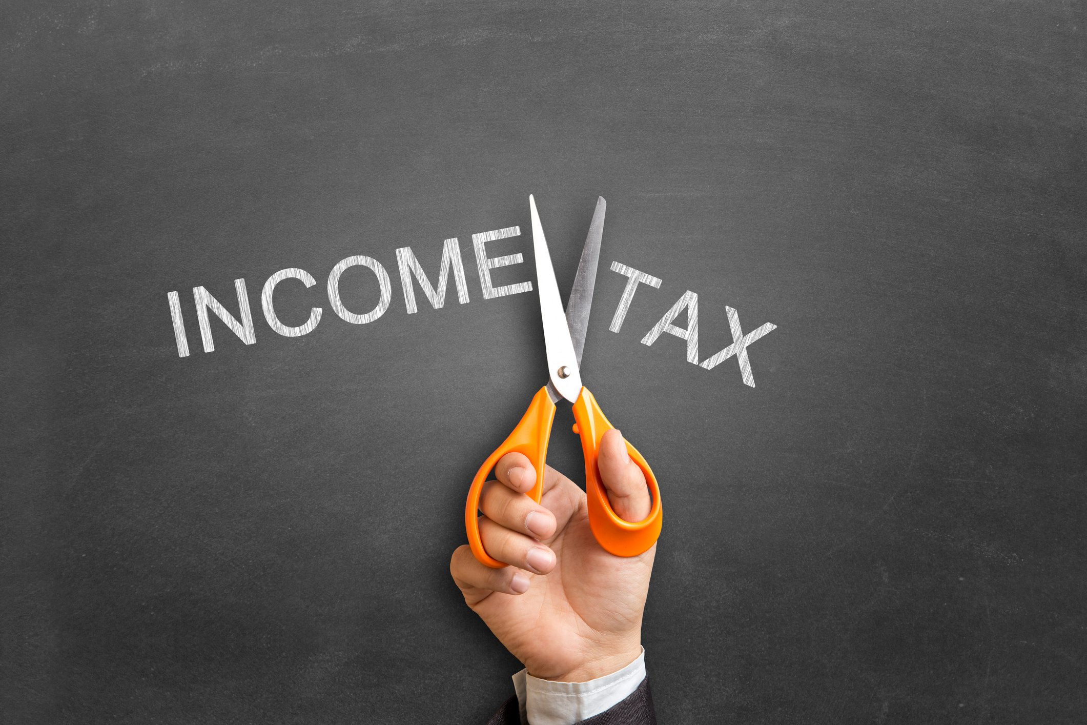 The words Income Tax written on a chalk board separated as a pair of scissors looks like it is cutting the phrase in two.