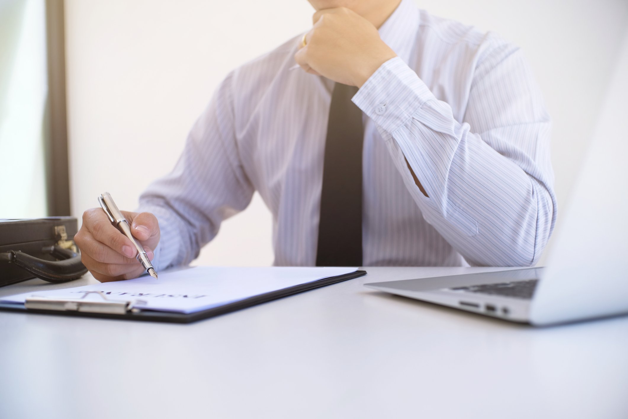 An investor considers a stock while writing on a clipboard and consulting a computer screen.