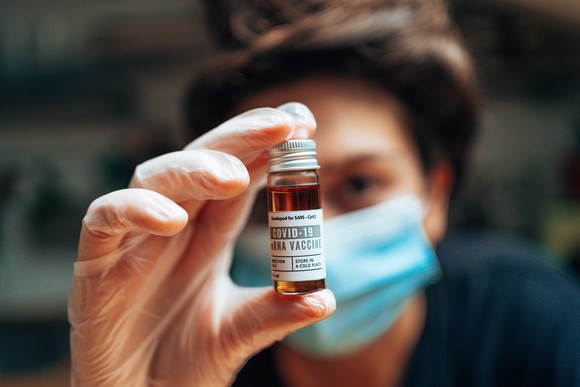 A clinician holds a vial labeled COVID-19 mRNA Vaccine.