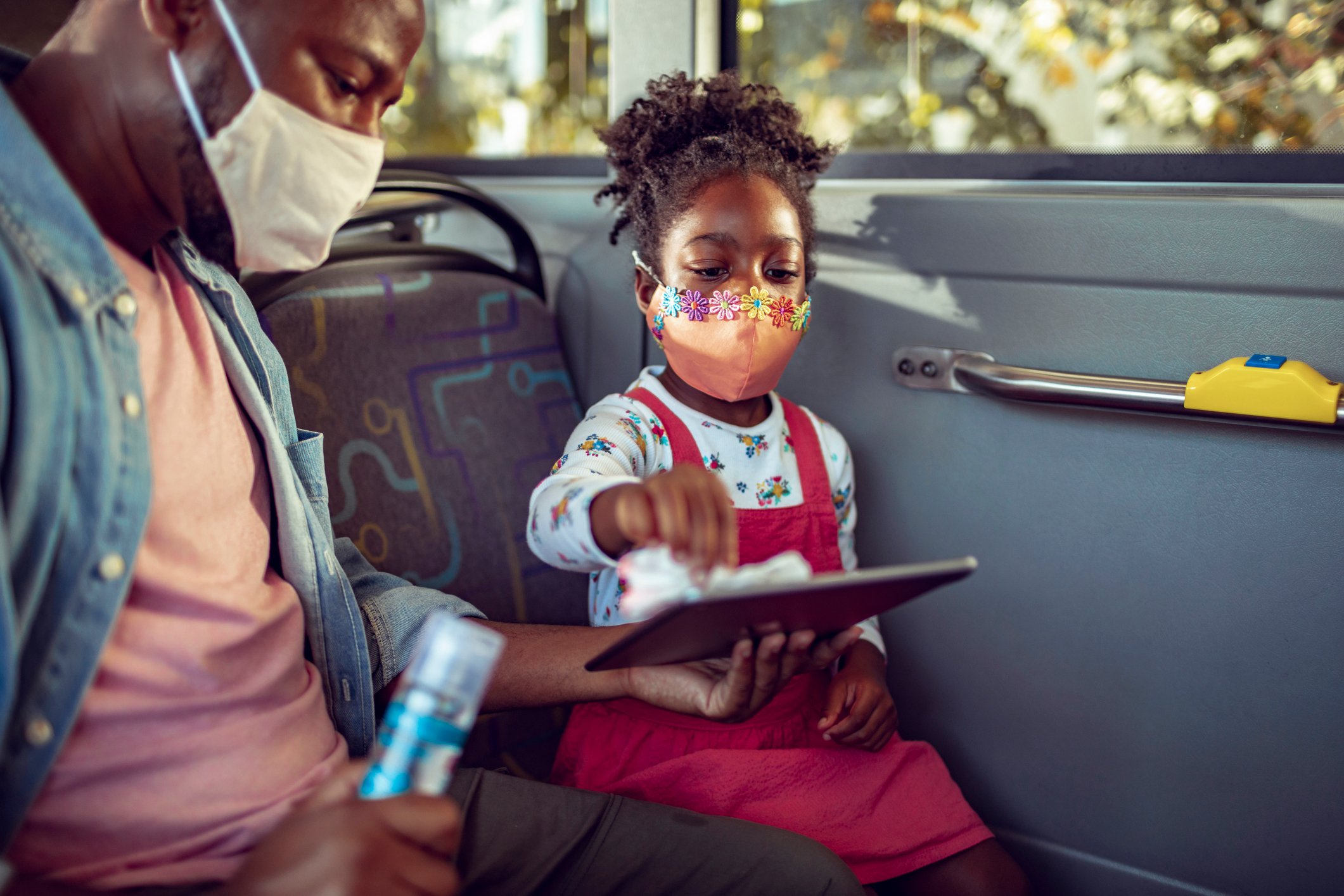 A man holds a tablet as his daughter cleans it with a wipe.