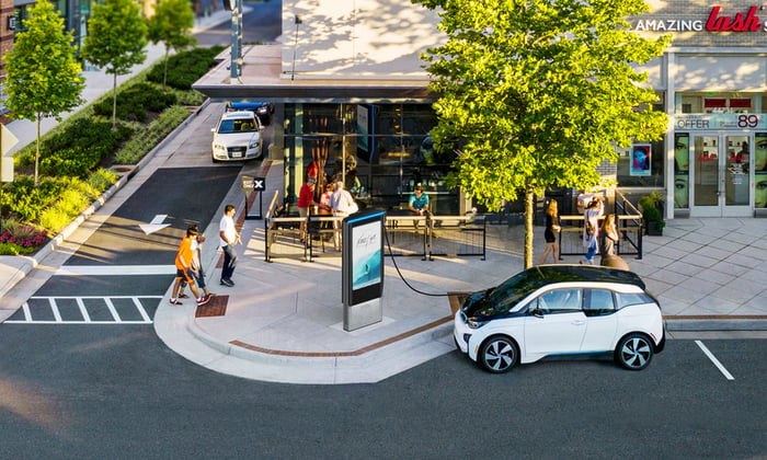 Car plugged into a Volta charging station on a retail shopping plaza, with a large screen showing advertising.