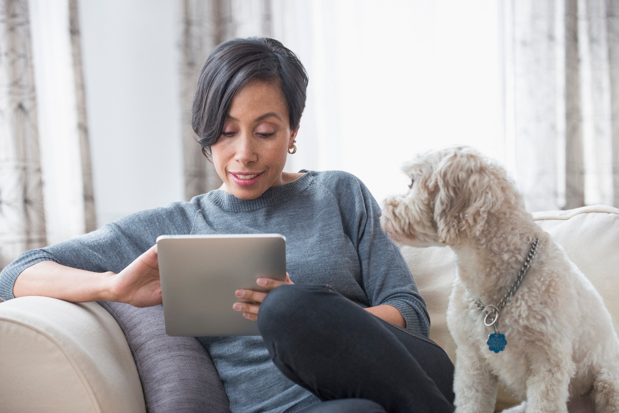 A woman sitting next to her dog and using a tablet.