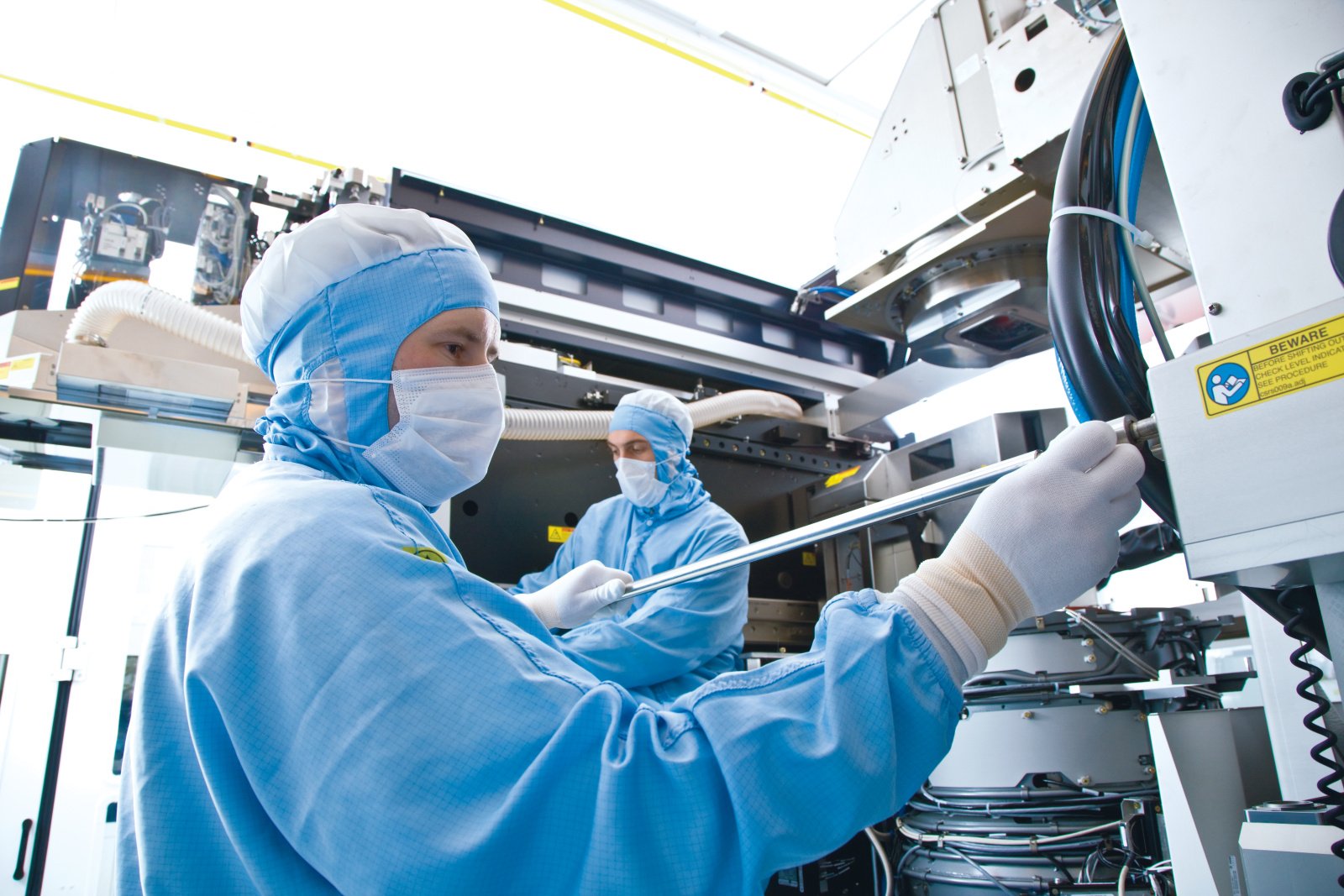 A technician works in a cleanroom with a semiconductor assembly machine.