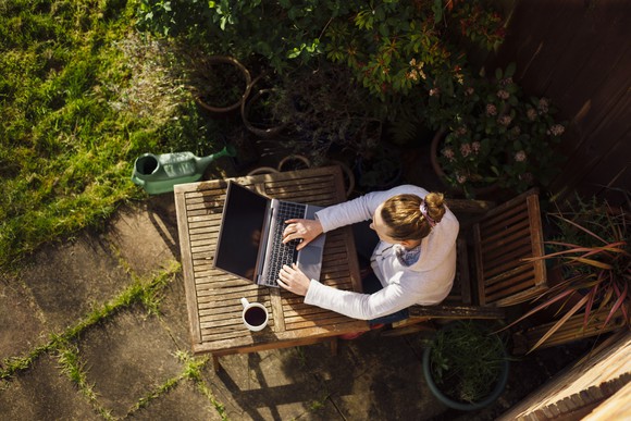Lady sitting on wooden chair and typing on a laptop placed on a wooden table