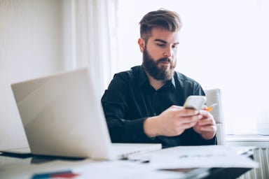 young man looks at phone while sitting at desk