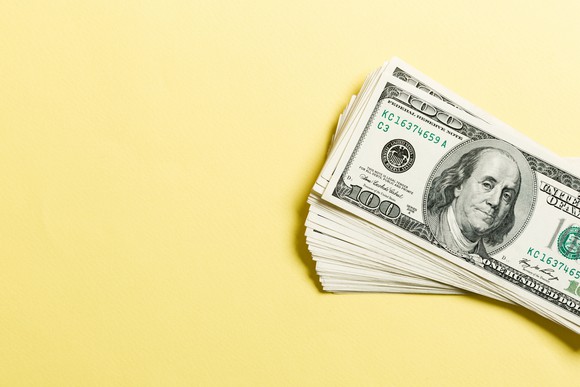 Stack of hundred dollar bills against a yellow background