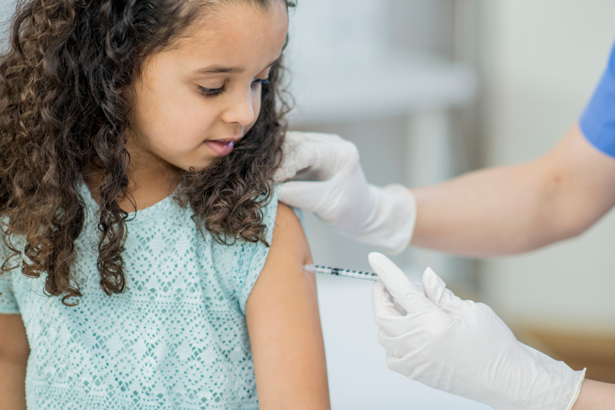A gloved healthcare worker vaccinates a little girl.