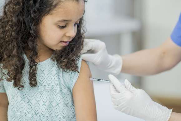 A gloved healthcare worker vaccinates a little girl.