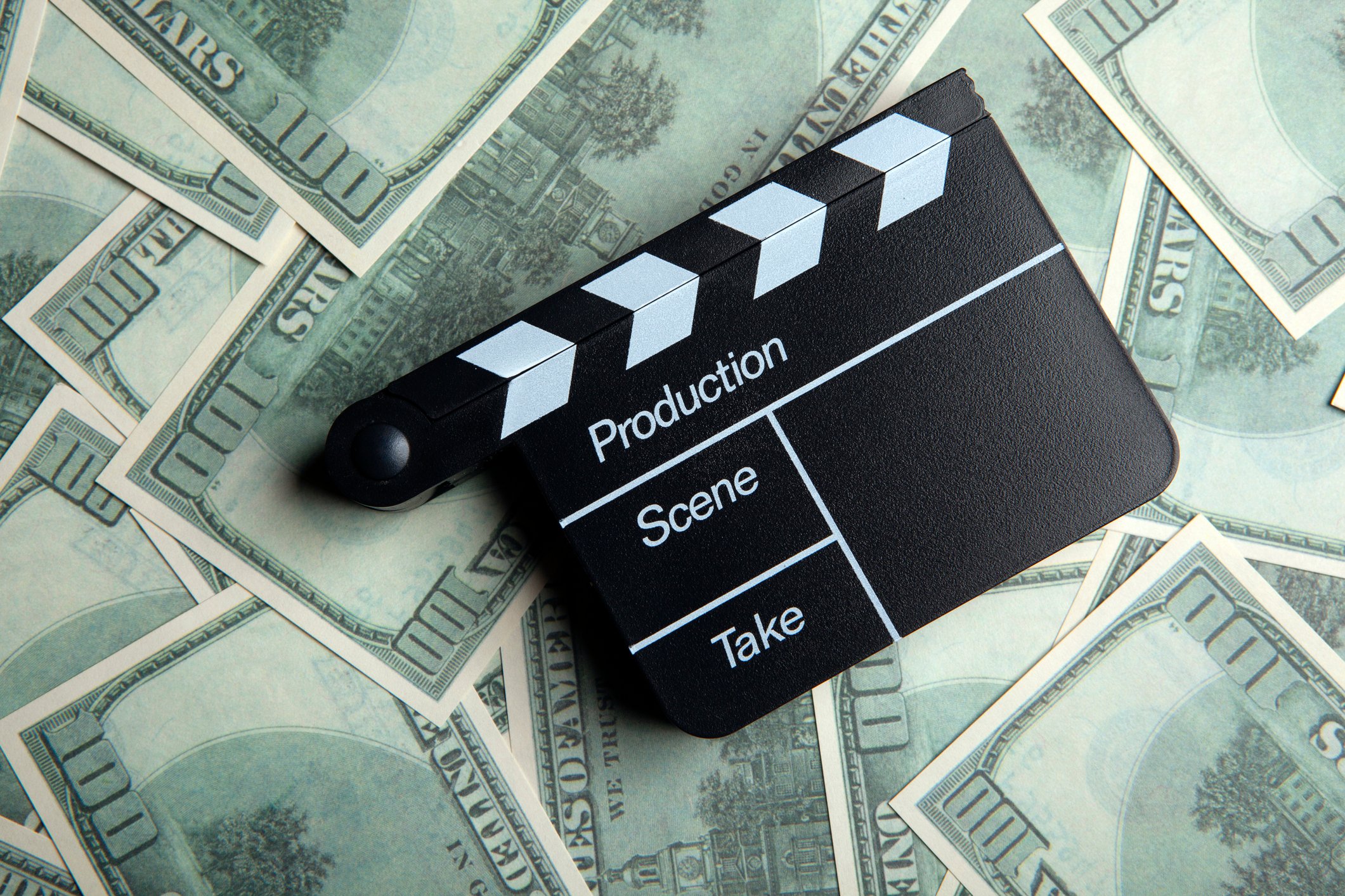 A movie director's clapper resting on a large pile of hundred-dollar bills.