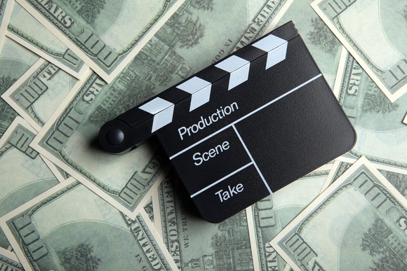 A movie director's clapper resting on a large pile of hundred-dollar bills.