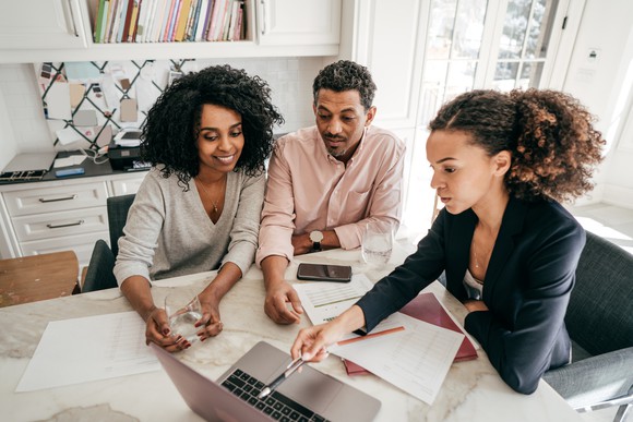 Three investors sit in front of a laptop and discuss stocks.