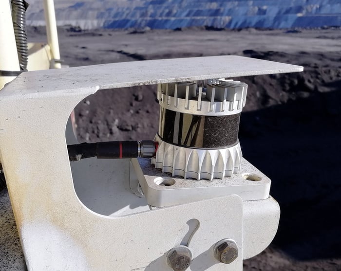 An Ouster lidar sensor, pictured with a mining operation in the background. 