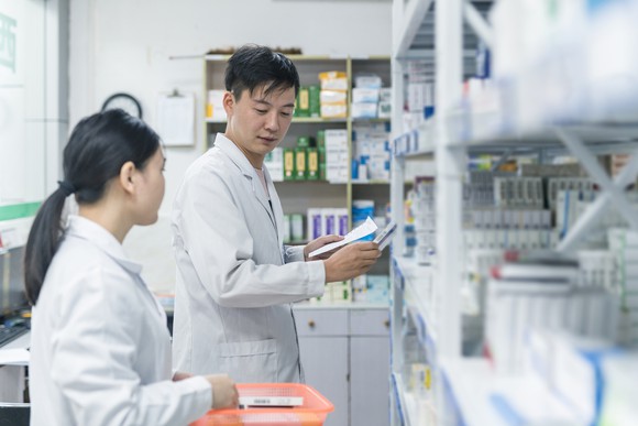 Two pharmacists look at shelves of medication.