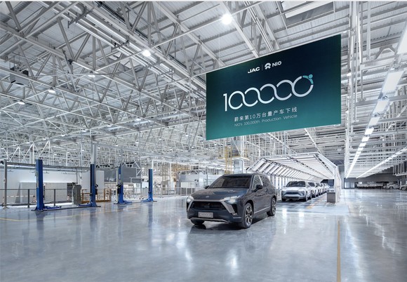 A blue NIO ES8, an upscale electric SUV, rolls off a factory assembly line under a commemorative banner.  