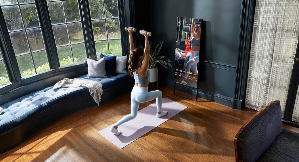 A woman lunges during a workout in front of a Mirror fitness device