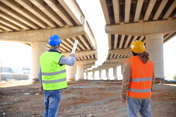 two construction workers look at the underside of a bridge under construction