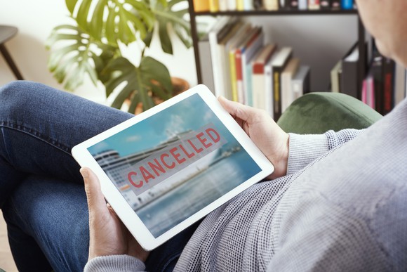 A man looking at a tablet, which shows an image of a cruise ship with "CANCELLED" superimposed over it in red lettering.