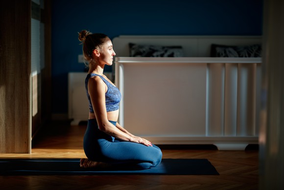 A woman in yoga apparel with her legs folded under her on a yoga mat.