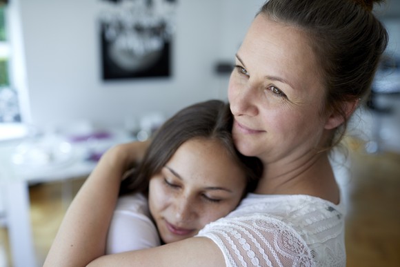 A mom hugs her teenage daughter in their living room.
