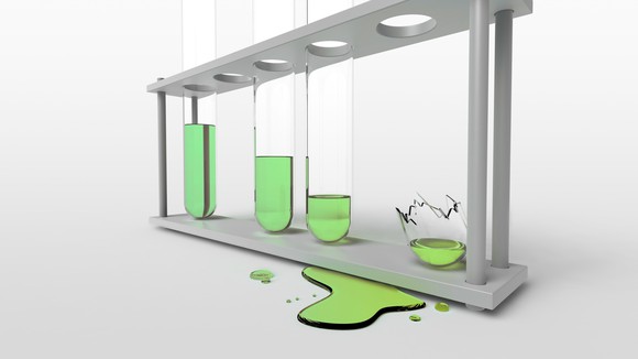 Test tube rack with a broken test tube spilling a green solution.