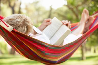 senior woman relaxing in hammock reading book