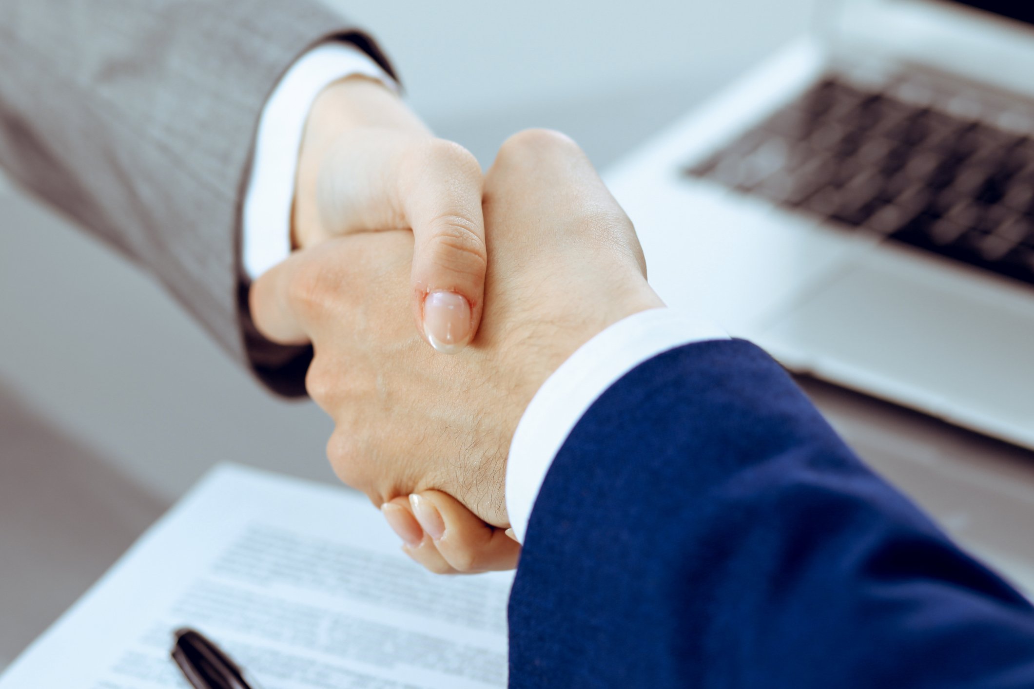 The hands of two executives shaking hands over a freshly signed contract. 
