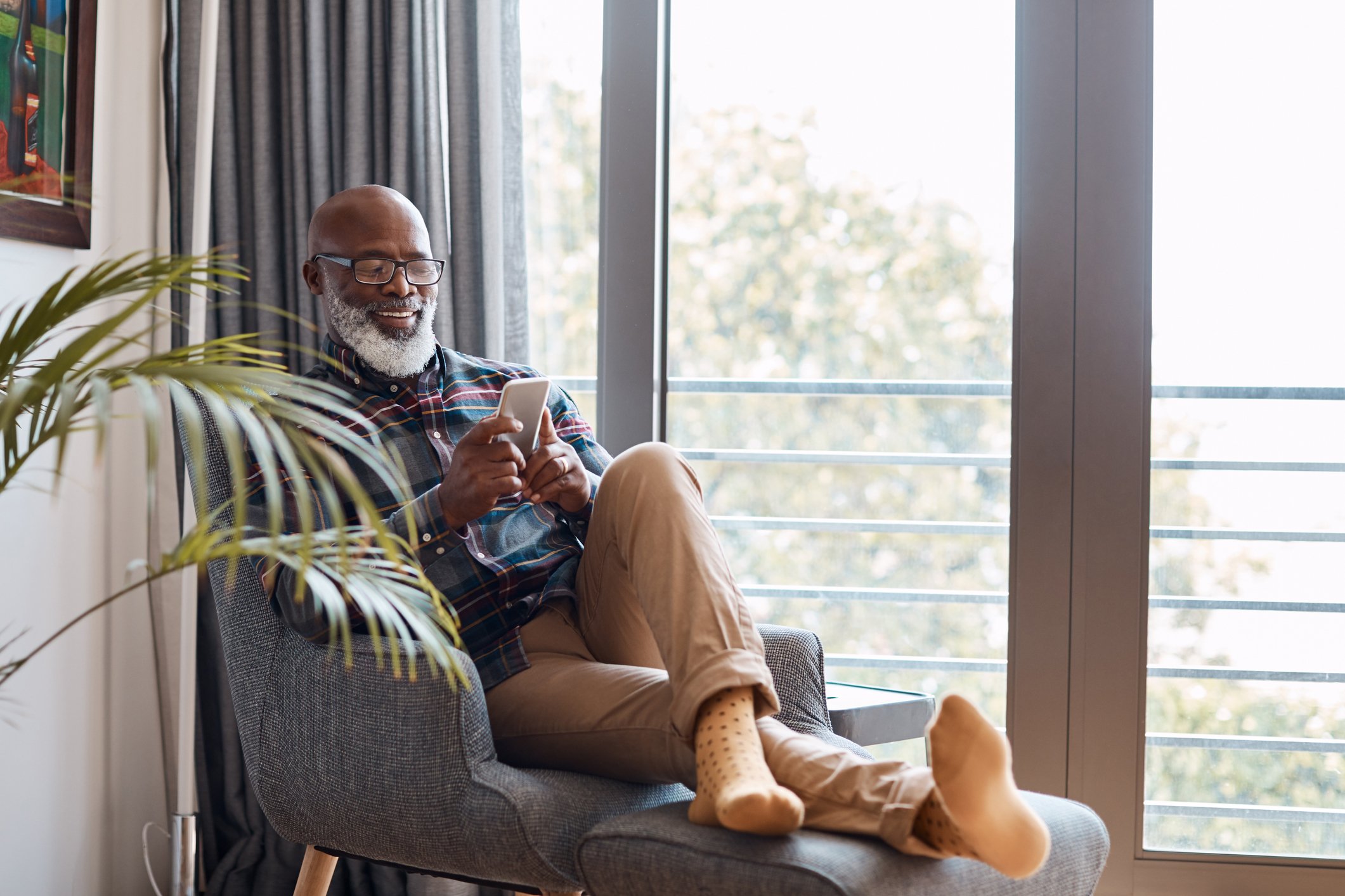 Man relaxing in a chair at home as he checks his smartphone.