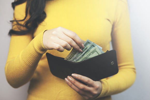 A woman reaches into her wallet for $100 bills.