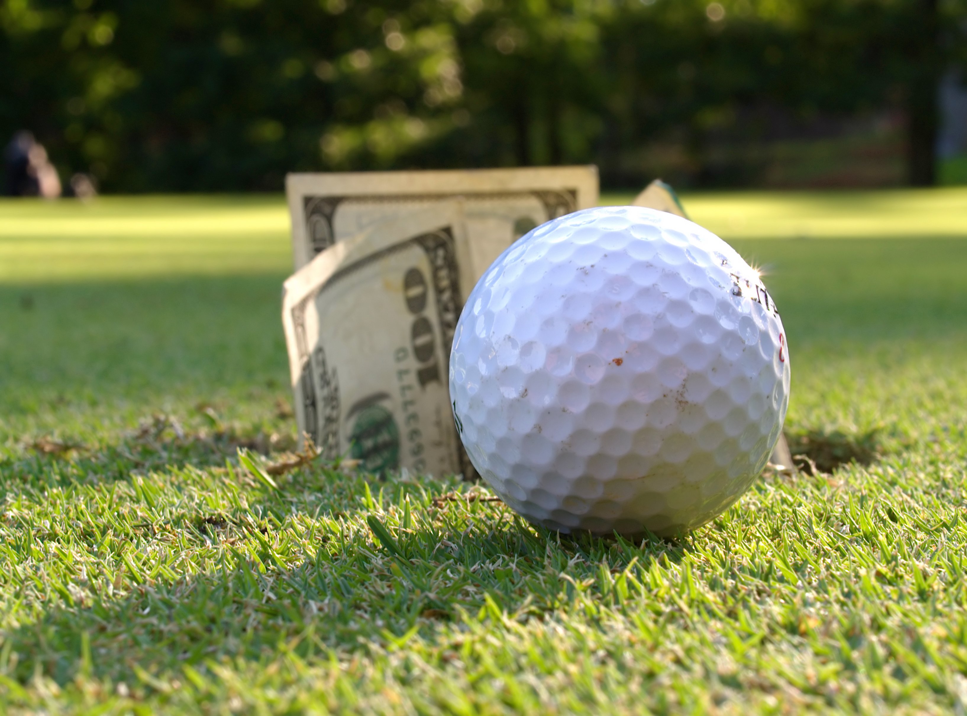 Ground-level view of golf ball on the green and $100 bills in the hole.