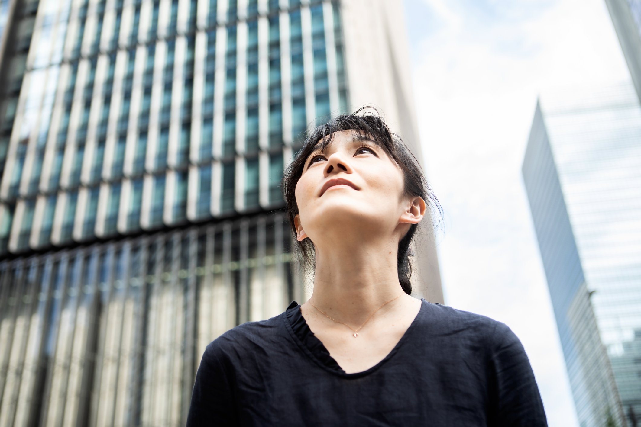A woman standing on a city street, looking up.