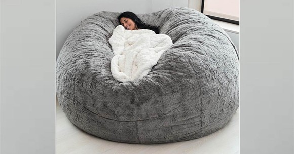 A woman resting with a blanket in a large Lovesac beanbag chair.