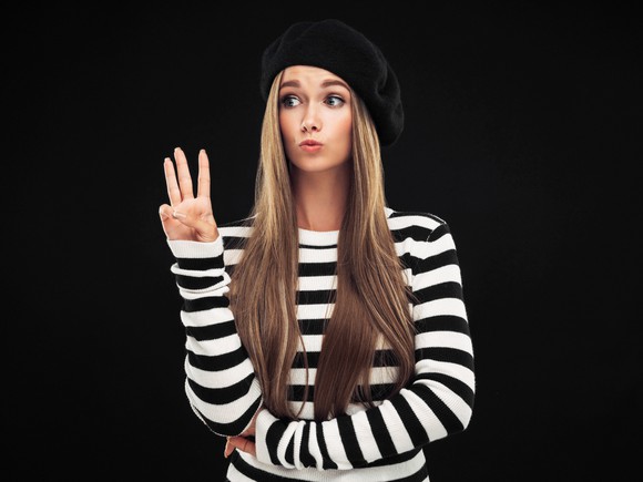 A woman wearing a black beret holding up three fingers.
