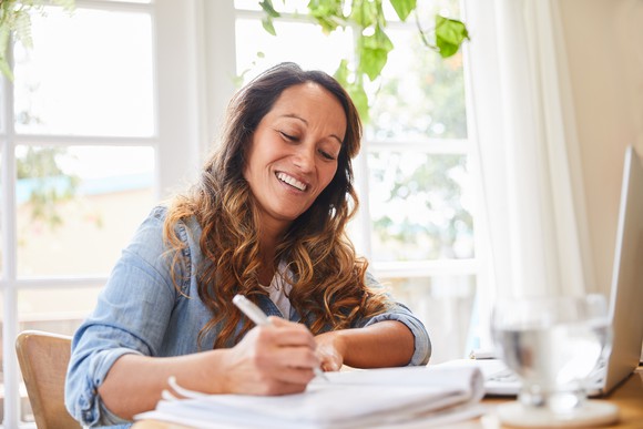 Woman at desk writing in notebook and smiling