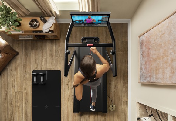 A view from above showing a young woman using a Peloton Tread treadmill in a home.