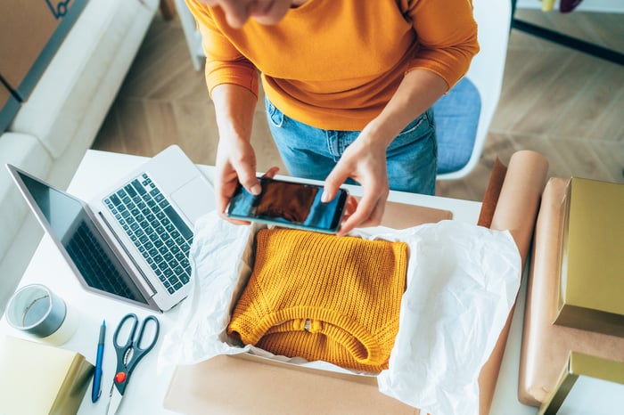 A person takes a photo of a yellow sweater folded into a box for shipping