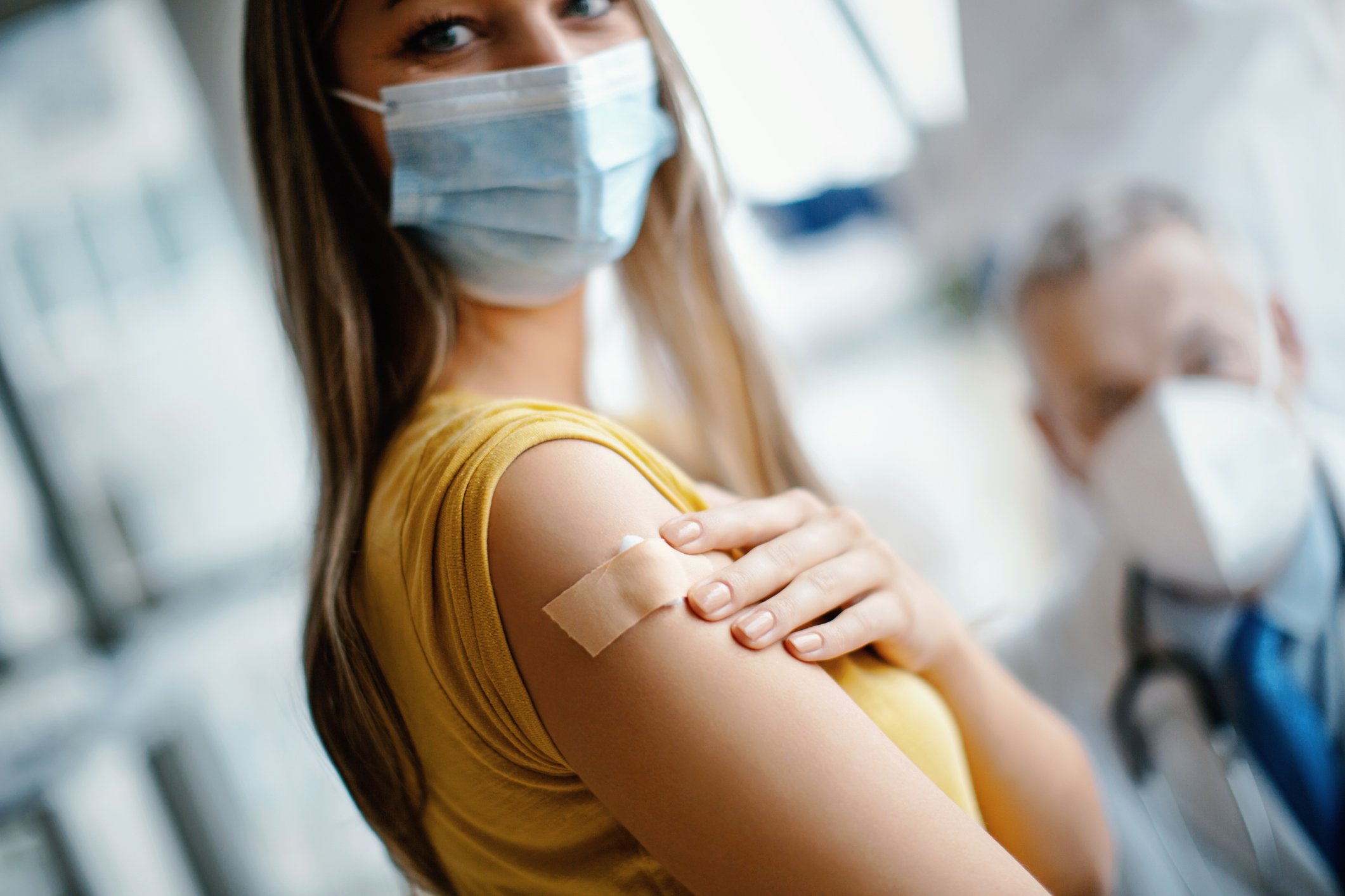 A masked woman looks into the camera and holds onto her arm after received a coronavirus vaccine.