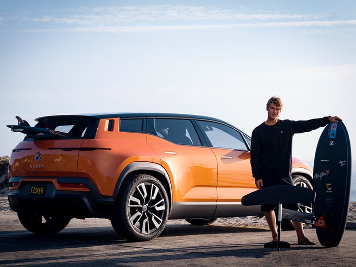 Orange Fisker Ocean SUV with surfer standing next to it