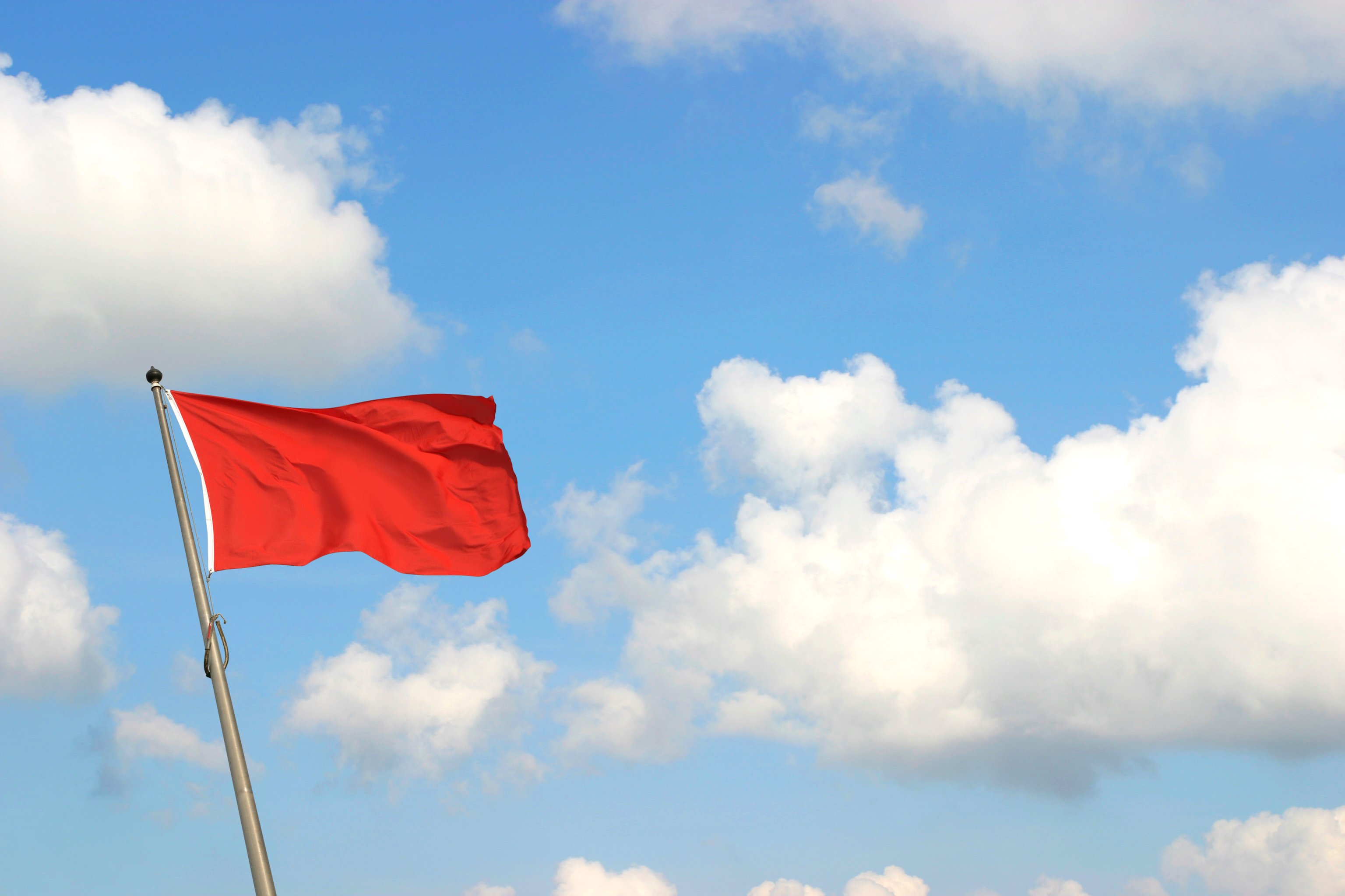 A red flag against clouds in the sky.