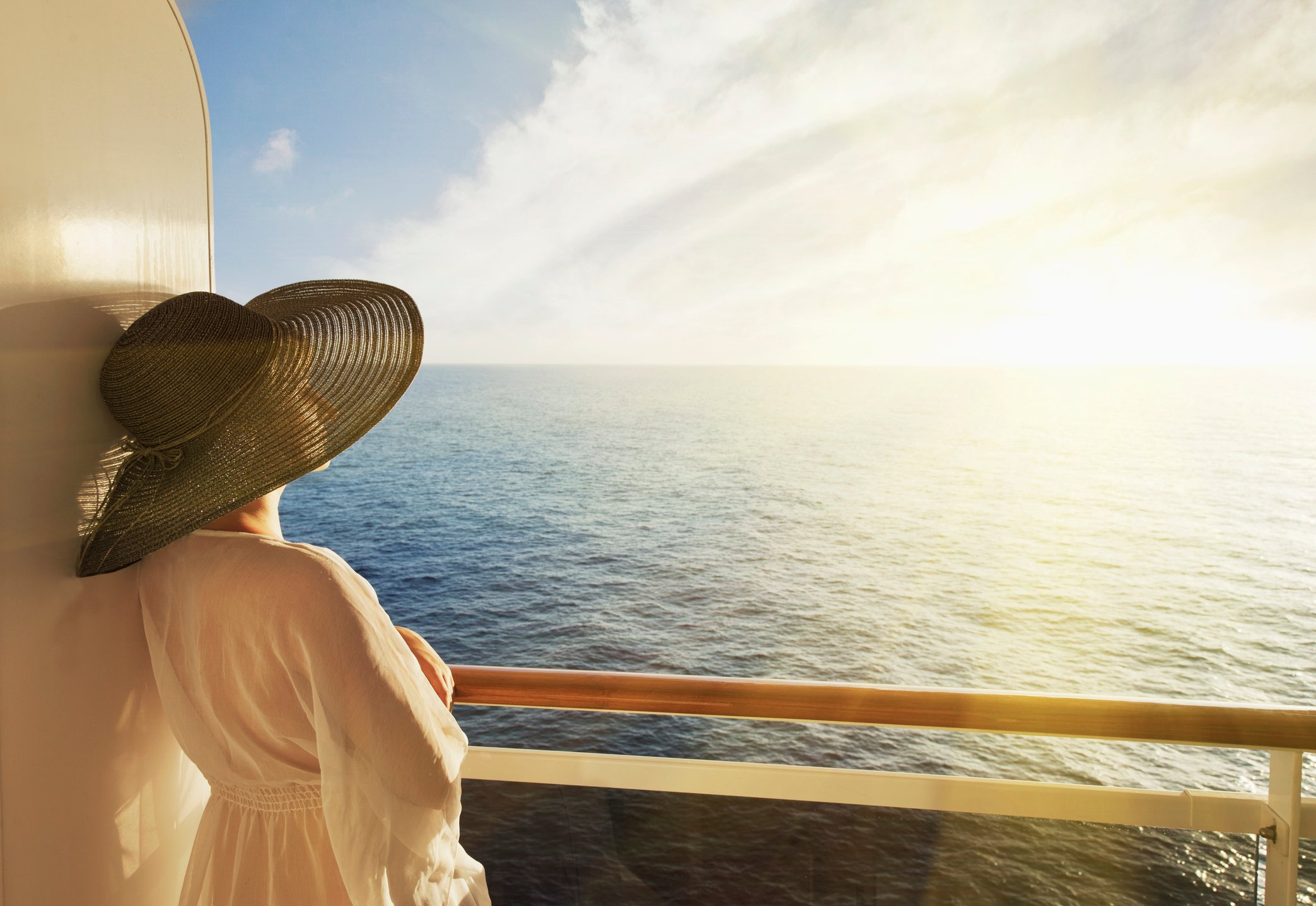 Woman in large hat standing on a cruise ship deck, looking out to sea.