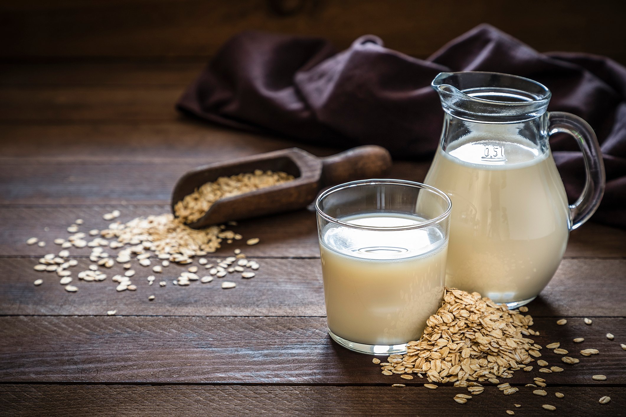A glass of oat milk and some oats laying on a table.