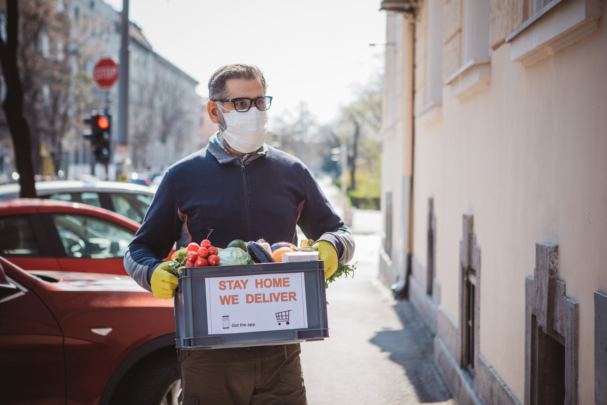 man with mask and gloves delivering box of food in city