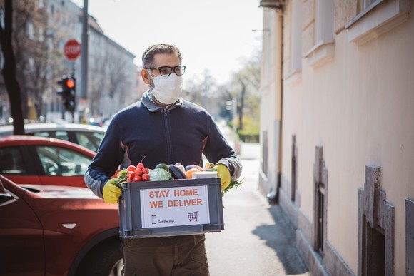 man with mask and gloves delivering box of food in city