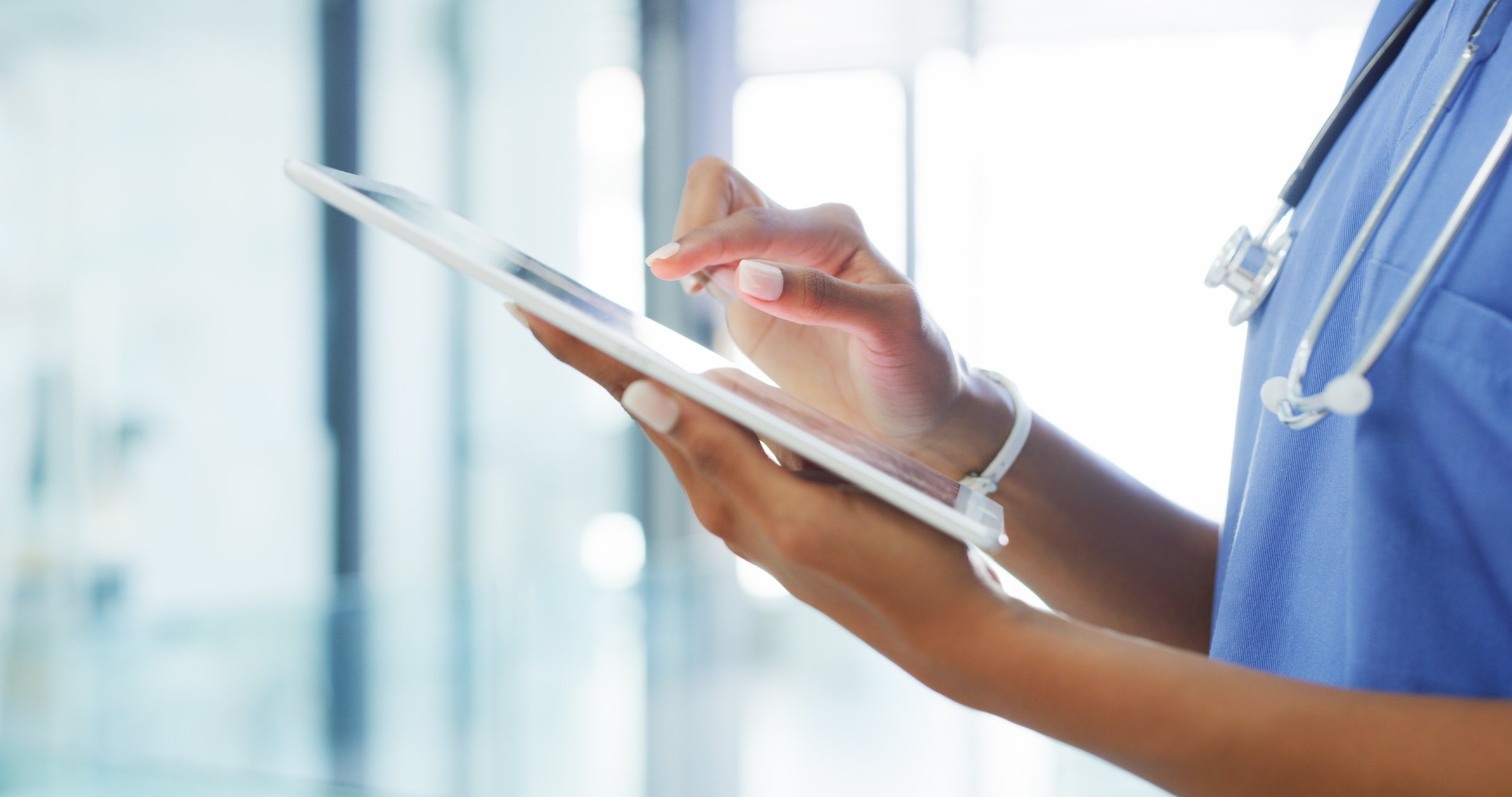 Person wearing scrubs and a stethoscope while using a tablet