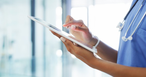 Person wearing scrubs and a stethoscope while using a tablet